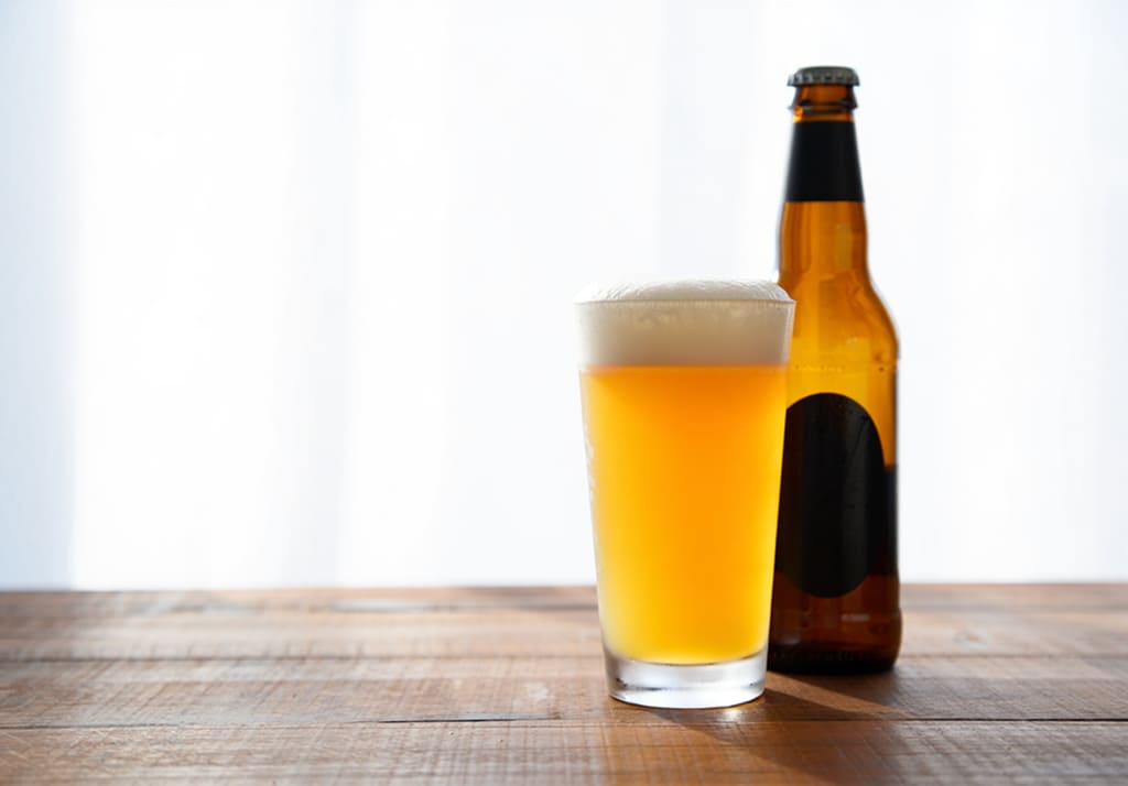 Стакан светлого пива с пеной и бутылка на деревянном столе